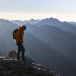 A solo traveler with a backpack stands on a mountain peak watching the sunrise, an inspiring image for an article about safe and memorable solo travel adventures.