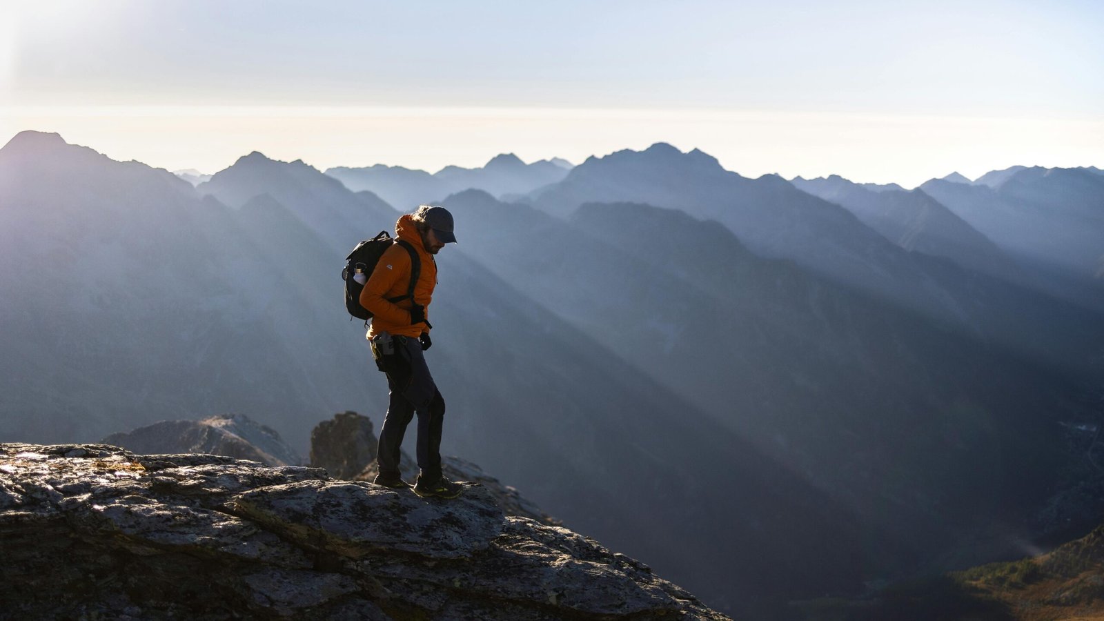 A solo traveler with a backpack stands on a mountain peak watching the sunrise, an inspiring image for an article about safe and memorable solo travel adventures.