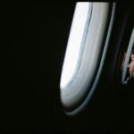 A young traveler looks out an airplane window at the wing and clouds, illustrating one of the key travel tips for first-time flyers: enjoying the journey.