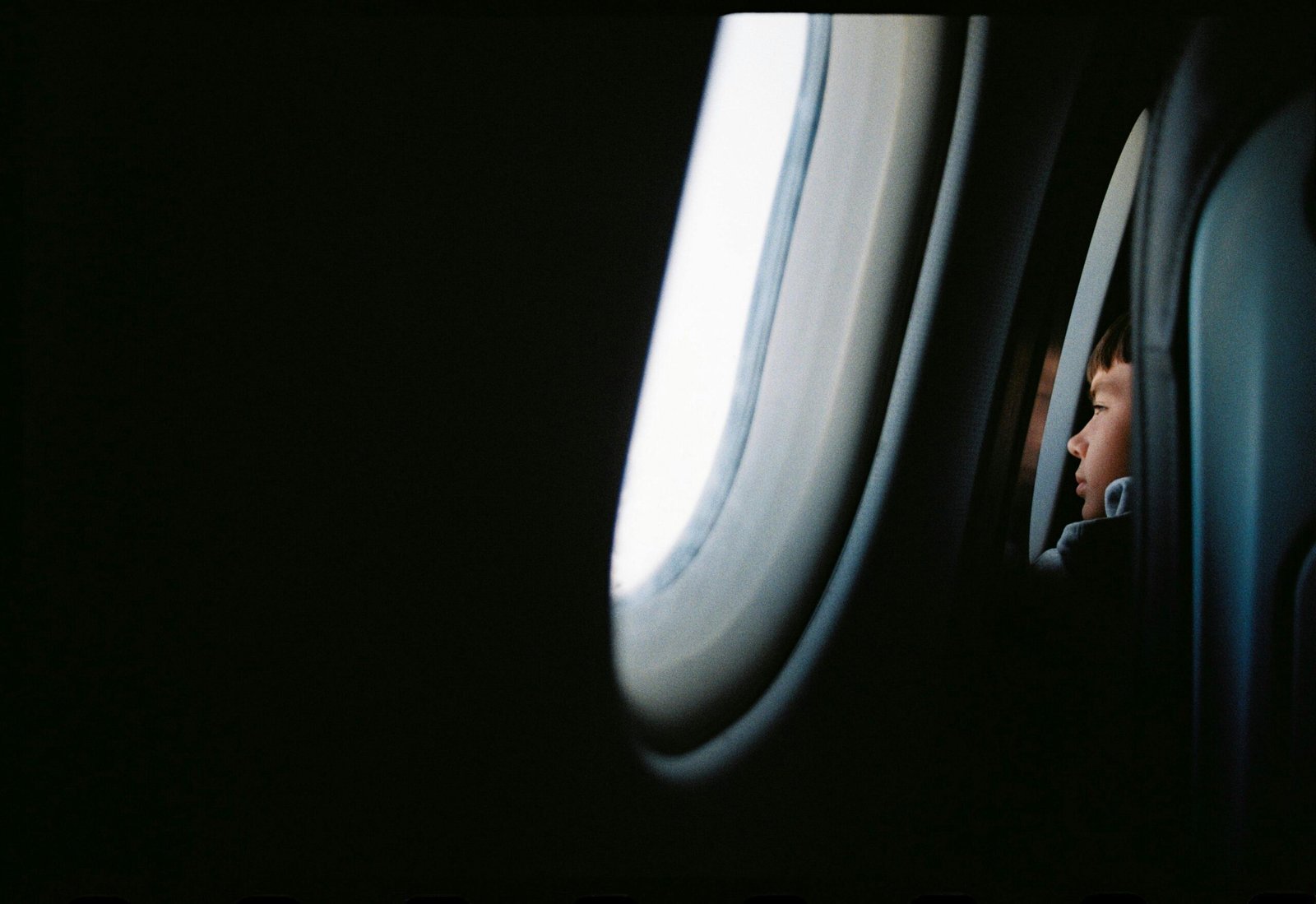 A young traveler looks out an airplane window at the wing and clouds, illustrating one of the key travel tips for first-time flyers: enjoying the journey.
