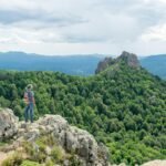 A solo traveler, seen from behind, stands on a scenic viewpoint overlooking a vast landscape, symbolizing freedom and self-discovery on an independent travel adventure.