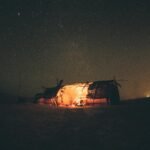 A beautiful Berber camp in the Moroccan Sahara desert at night, with glowing tents sitting on sand dunes under a clear, starry sky and the Milky Way.