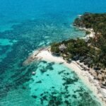Aerial view of a beautiful tropical island paradise with a white sand beach and turquoise ocean, illustrating the best island to visit for a 2025 vacation getaway.