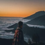 A solo traveler with a backpack looks out over a vast mountain landscape, illustrating the freedom and self-discovery of a well-planned solo travel journey.