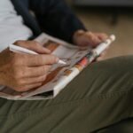 A person focused on a newspaper crossword puzzle with a pen, illustrating the process of solving a tricky clue like 'eat quickly with down'.