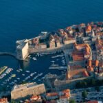 Scenic view of Croatia's ancient city walls overlooking the turquoise Adriatic Sea under a clear blue sky, illustrating the best time to travel to Croatia for an ideal getaway.